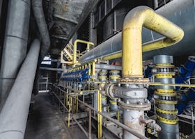 Close-up of an intricate industrial pipeline system featuring yellow valves and steel structures inside a factory.