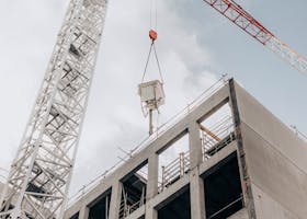 From below of modern hydraulic luffing jib tower crane working at construction site near modern unfinished multistory building under cloudy sky in city